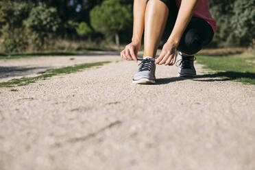 Woman tying shoelace on footpath - ABZF03528