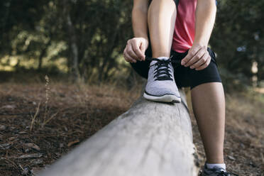 Woman tying shoelace while sitting on tree trunk in forest - ABZF03529