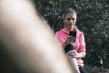 Sportswoman using smart phone in forest - ABZF03530