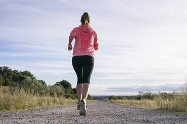 Female runner jogging on country road during sunny day - ABZF03532