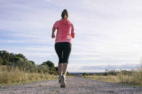 Weibliche Läuferin beim Joggen auf der Landstraße an einem sonnigen Tag - ABZF03532