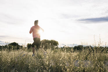 Weibliche Joggerin, die an einem sonnigen Tag durch ein landwirtschaftliches Feld läuft - ABZF03534