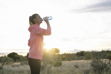 Female runner drinking water from bottle during sunset - ABZF03537