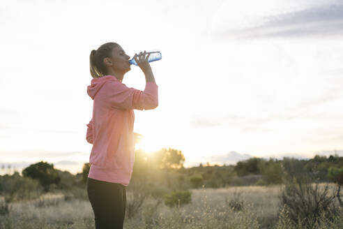 Läuferin trinkt bei Sonnenuntergang Wasser aus einer Flasche - ABZF03537