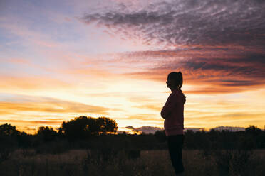 Woman standing in agricultural field during sunset - ABZF03542