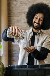Smiling male gardener pouring seeds from glass jar at workshop - AFVF08561