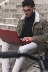 Male entrepreneur with eyeglasses working on laptop while sitting on steps - JAQF00464