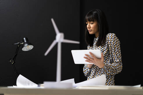 Businesswoman using digital tablet by black wall at office - GIOF12339