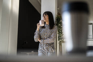 Female professional looking away holding mug during coffee break at office - GIOF12344