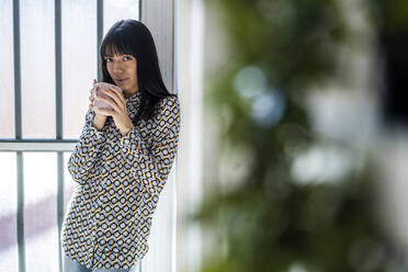 Female professional holding mug while leaning on wall - GIOF12346