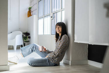 Businesswoman with mug leaning by column at office during sunny day - GIOF12348