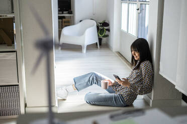 Berufstätige Frau benutzt ihr Smartphone, während sie sich im Büro an eine Säule lehnt - GIOF12349
