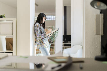 Businesswoman leaning on column while holding notebook - GIOF12357