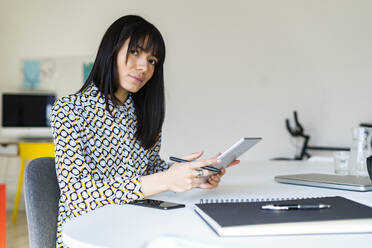 Female professional holding graphic tablet at desk in office - GIOF12360