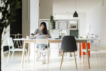 Female entrepreneur with graphic tablet sitting on desk at office - GIOF12361