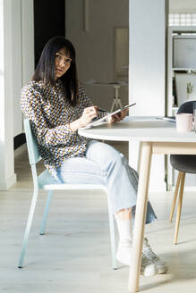 Weibliche Fachkraft mit Grafiktablett sitzt auf einem Stuhl im Büro - GIOF12362