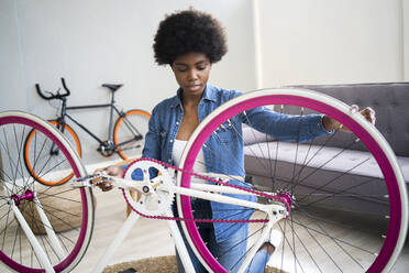 Afro hairstyle woman repairing bicycle at home - GIOF12391