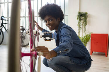 Smiling Afro hairstyle woman repairing bicycle at home - GIOF12392