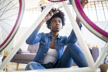 Afro woman holding work tool while repairing bicycle at home - GIOF12399