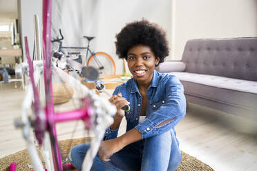 Glückliche junge Frau repariert Fahrrad zu Hause - GIOF12400