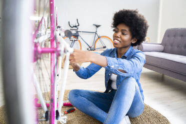 Smiling woman enjoying bicycle repairing at home - GIOF12401