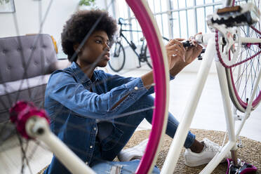 Concentrated woman with Afro hairstyle repairing bicycle at home - GIOF12402