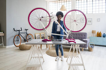 Smiling young woman with bicycle on table at home - GIOF12406