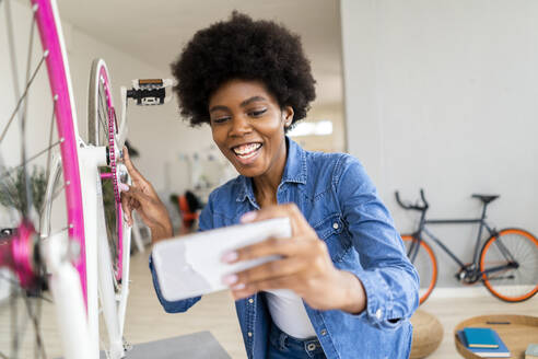 Weibliche Influencerin lächelt, während sie zu Hause über ihr Handy vloggt - GIOF12419