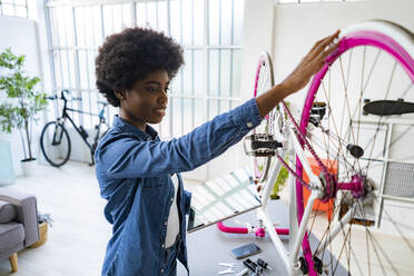 Smiling woman repairs bike while using digital tablet at home - GIOF12425