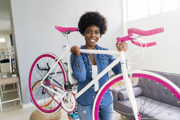 Smiling young woman carrying bicycle at home - GIOF12433