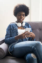 Junge Frau benutzt Handy auf dem Sofa zu Hause - GIOF12440