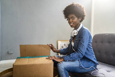 Lächelnde junge Frau beim Auspacken eines Pakets im heimischen Wohnzimmer - GIOF12442