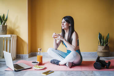 Beautiful woman looking away while having juice at home - EBBF03317