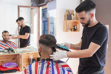 Männlicher Friseur, der einer Kundin mit einer Maschine im Salon die Haare schneidet - JRVF00407