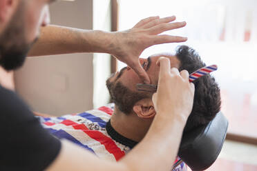 Ein männlicher Friseur trimmt den Bart eines Mannes mit einem Rasiermesser im Salon - JRVF00409