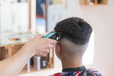 Männlicher Friseur benutzt eine Maschine, um die Frisur eines Teenagers zu stylen - JRVF00413