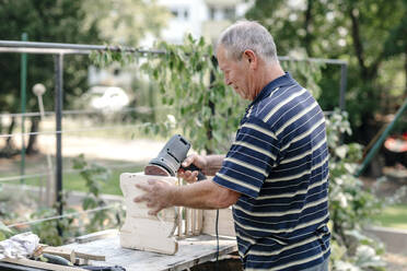 Aktiver älterer Mann mit Holzbearbeitungswerkzeug bei Tischlerarbeiten im Hinterhof - OGF01023