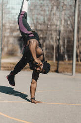 African man doing handstand while talking on mobile phone during sunny day - GUSF05737