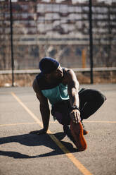 Junger Mann streckt seine Hand auf einem Basketballplatz an einem sonnigen Tag - GUSF05739