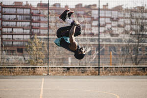 Young man practicing acrobats on sports court during sunny day - GUSF05740