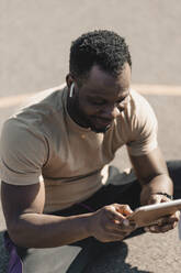 African man using digital tablet while listening music through wireless headphones - GUSF05744