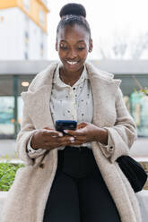 Lächelnde afrikanische Frau, die im Freien ein Mobiltelefon benutzt - JRVF00419