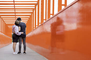 Teenager-Paar, das sich auf einer orangefarbenen Brücke umarmt - PSTF00946