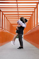 Teenage boy picking up girlfriend on orange bridge - PSTF00947