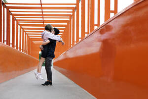 Teenager-Paar küsst sich auf orangefarbener Brücke - PSTF00948