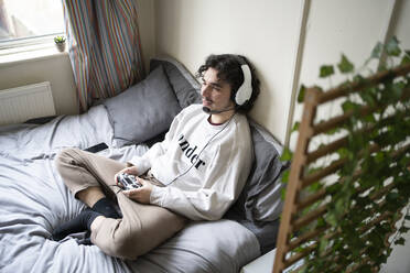 Young man with headphones playing video game at home - FBAF01783