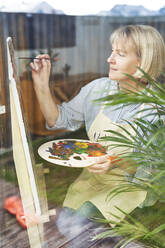 Schöne Frau macht Zeichnung durch Pinsel auf Staffelei zu Hause - ABIF01365