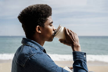 Man drinking coffee at beach during sunny day - AFVF08586