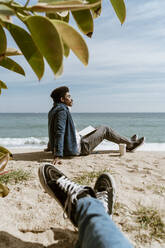 Entspannter Mann mit Buch am Strand sitzend an einem sonnigen Tag - AFVF08587