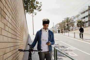 Handsome man using mobile phone while standing with bicycle on footpath - AFVF08592